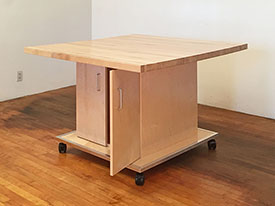 Rolling table for the art studio has adjustable shelving for stoing art supplies and art supply papers.