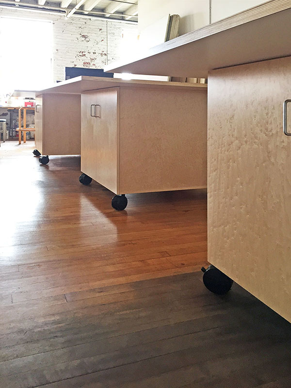 Art Studio Furniture by Art Boards™. Rolling library work tables have adjustable shelving behind maple doors. The counter tops are 1" thick with a white laminate surface. The library table is 60" x 60", it has 13" overhang on all sides for knee space when sitting.